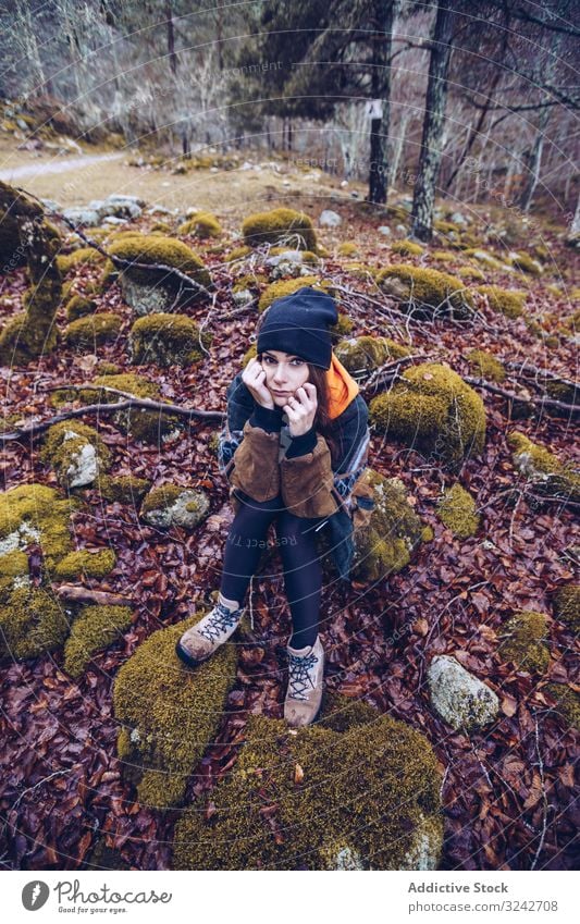 Gelangweilte Touristin ruht sich auf Felsen im Herbstwald aus ruhen Wald gelangweilt sitzen Stein Frau getrocknet Laubwerk braun Moos auf die Hand gestützt Hut