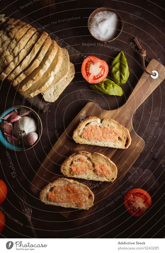 Gewürze und Gemüse in der Nähe von Toast Zuprosten Saucen Bestandteil Tomate Salz Knoblauch Basilikum Erdöl Brot Schneidebrett Tisch Lebensmittel Snack lecker