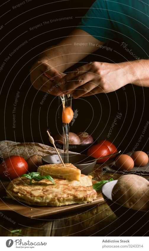 Erntehelfer bricht Ei in der Nähe von Kuchen Mann Pause Koch Bestandteil Pasteten Tortilla Lebensmittel Tisch rustikal dunkel Küche lecker geschmackvoll