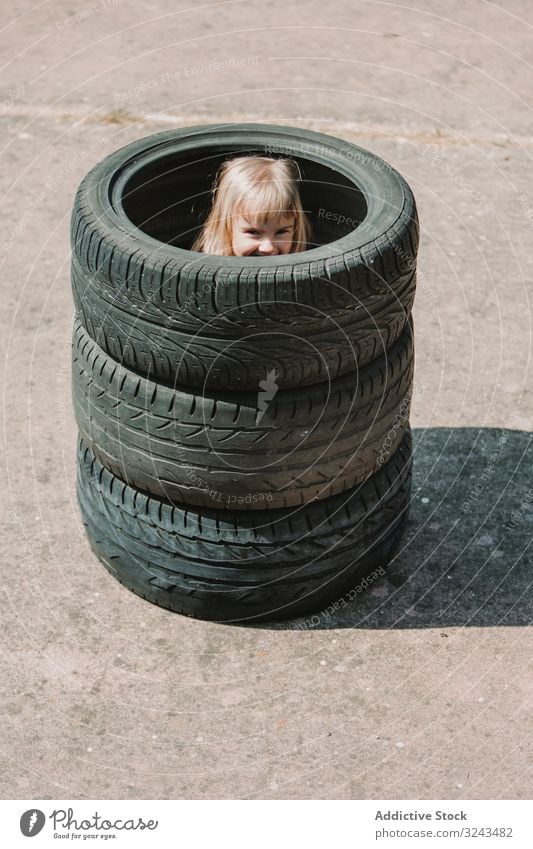 Kleines Mädchen versteckt sich im Reifenstapel Kind unanständig Spaß spielen Streich Stapel wenig Glück Freude Kindheit aktiv heiter Freizeit Lächeln Lachen