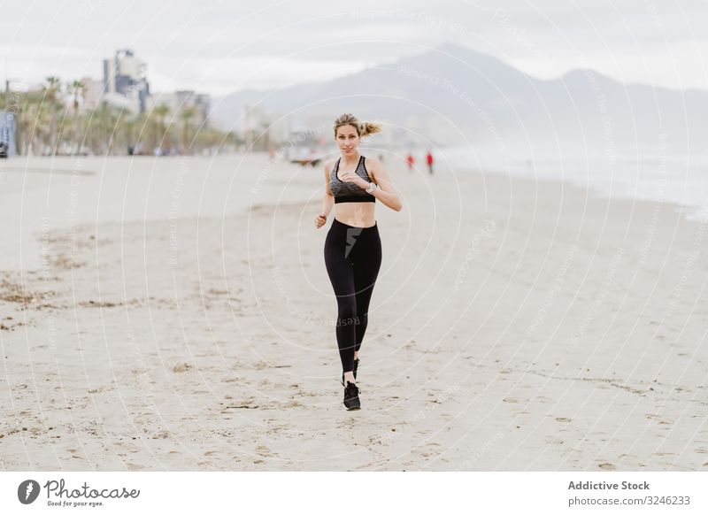 Läuferin in modischer Sportkleidung joggt an ruhiger, sandiger Küste Frau Joggen Strand springend Sommer Gesundheit ausarbeitend Übung Meer Aktivität Training