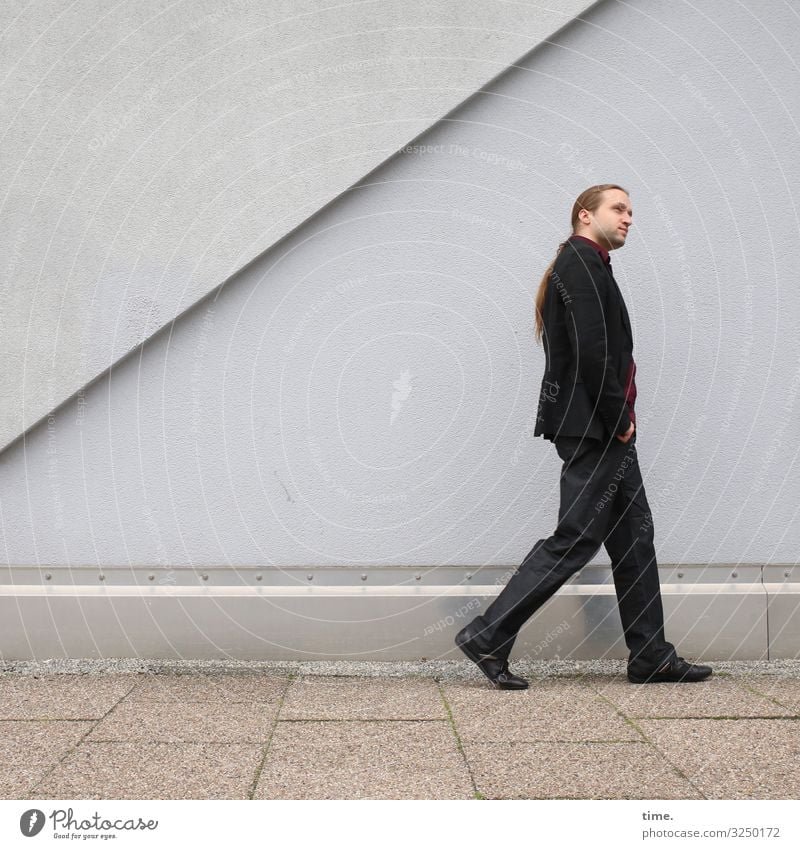 Schlendermodus maskulin Mann Erwachsene 1 Mensch Mauer Wand Wege & Pfade Bürgersteig Anzug brünett langhaarig Zopf Dreitagebart beobachten festhalten gehen