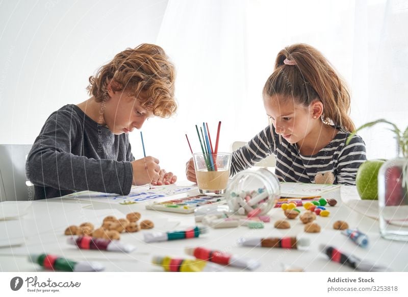 Fokussierte Kinder malen am Tisch Farbe Wasserfarbe Pinselblume fokussiert Freund heimwärts Kunst kreativ Bildung sitzen Zusammensein Mädchen Junge Pigment