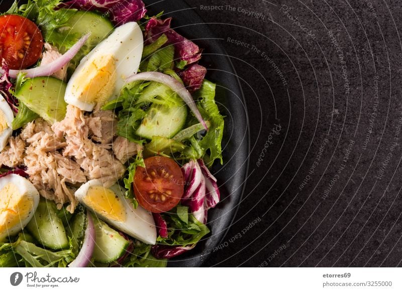 Salat mit Thunfisch, Ei und Gemüse auf schwarzem Hintergrund Salatbeilage Tomate Kopfsalat Teller Zwiebel Gurke Salatgurke Scheibe gemischt Olivenöl