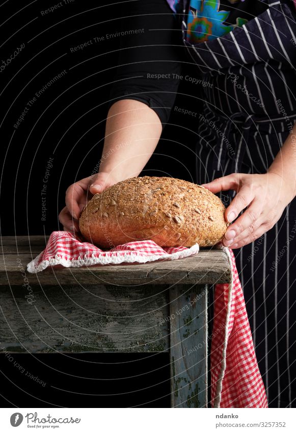 Frau hält in ihren Händen gebackenes Rundbrot Teigwaren Backwaren Brot Tisch Küche Mensch Erwachsene Hand Holz machen dunkel frisch braun schwarz weiß Tradition