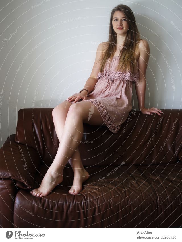 Portrait einer jungen Frau auf einer braunen Couch elegant Stil Freude schön Leben Sofa Raum Junge Frau Jugendliche Beine 18-30 Jahre Erwachsene Kleid Barfuß