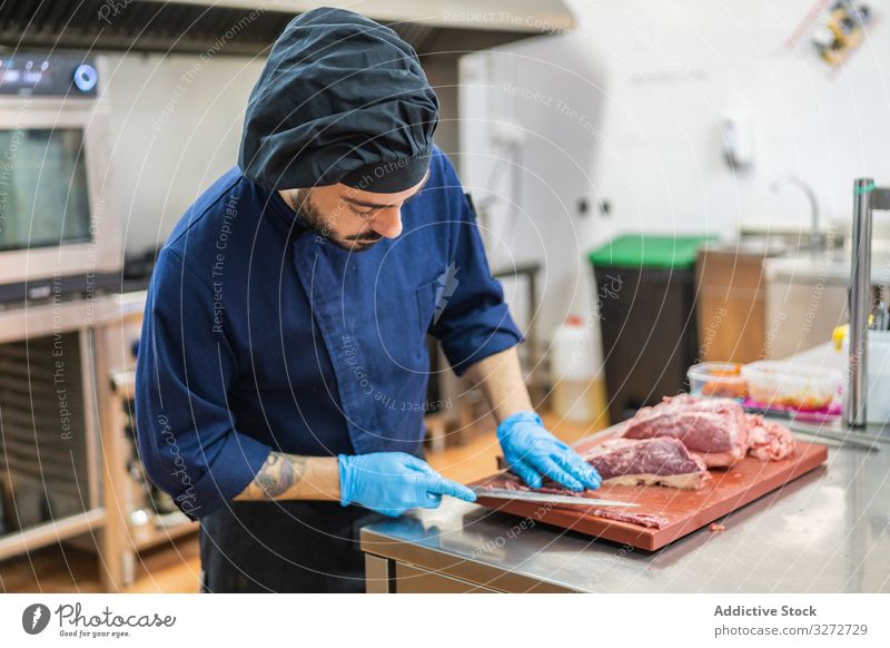 Chefkoch schneidet Fleisch in der Küche Küchenchef geschnitten Scheibe roh Mann vorbereiten Koch professionell Schneidebrett Messer Tisch Beruf männlich