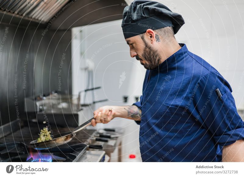 Koch, der Gemüse auf dem Gasherd brät Küchenchef Arbeit Bratpfanne braten Speise Mann professionell Herd Flamme vorbereiten schütteln Uniform Hut Erwachsener