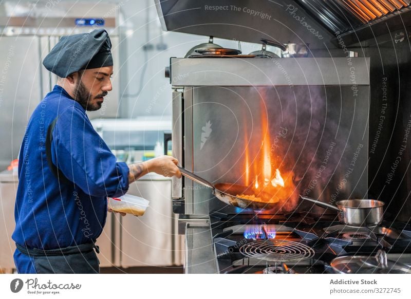 Koch, der mit Flamme in der Pfanne kocht Küchenchef Arbeit Feuer Bratpfanne braten Speise Mann professionell flambieren heiß Herd Gas vorbereiten Uniform Hut