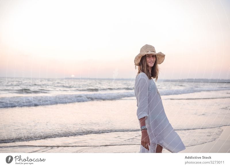 Charmante Frau in hellem weißen Kleid schaut über die Schulter in die Kamera am welligen Strand MEER reisend Lehnen Seeküste Tourismus charmant Urlaub Hut