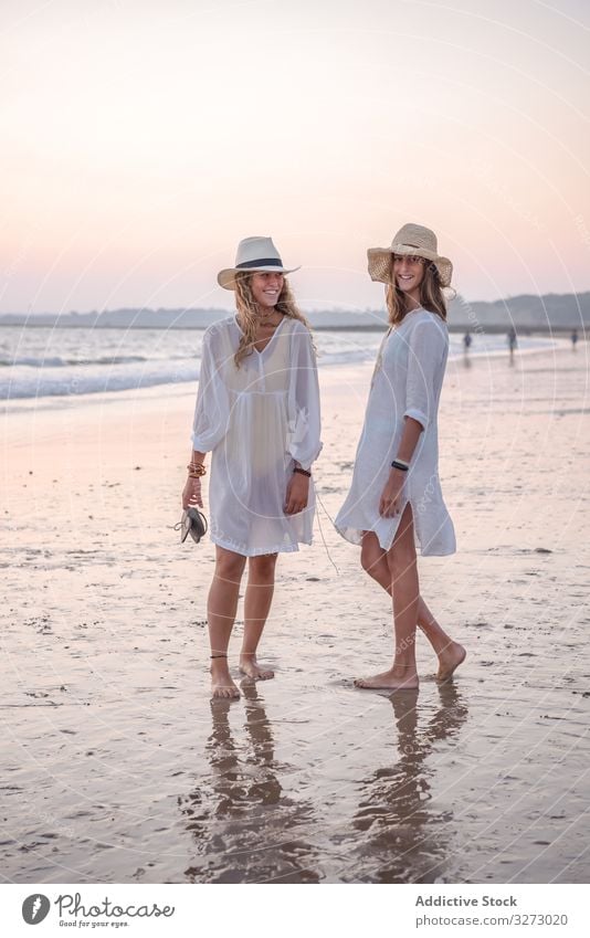 Lächelnde Freundinnen in Sommerkleidung barfuss im Wasser am Strand Frauen MEER Barfuß reisend Seeküste charmant Urlaub Hut lockig Feiertag Zusammensein