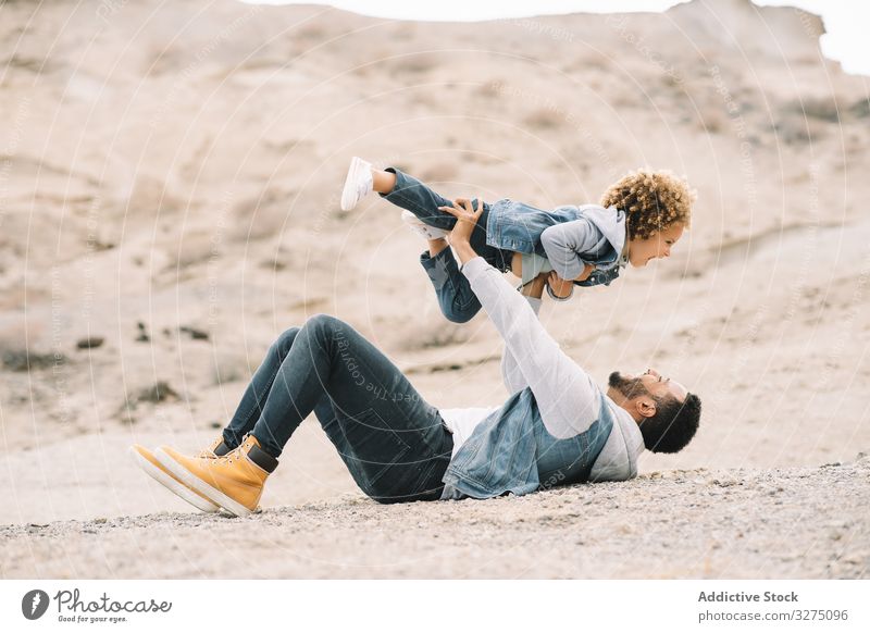 Ethnischer Vater spielt mit Kind am Boden Kleinkind spielen Spaß ruhen Sand Hügel Lächeln Eltern Glück heiter Lifestyle modern Natur Papa Mann horizontal Bonden