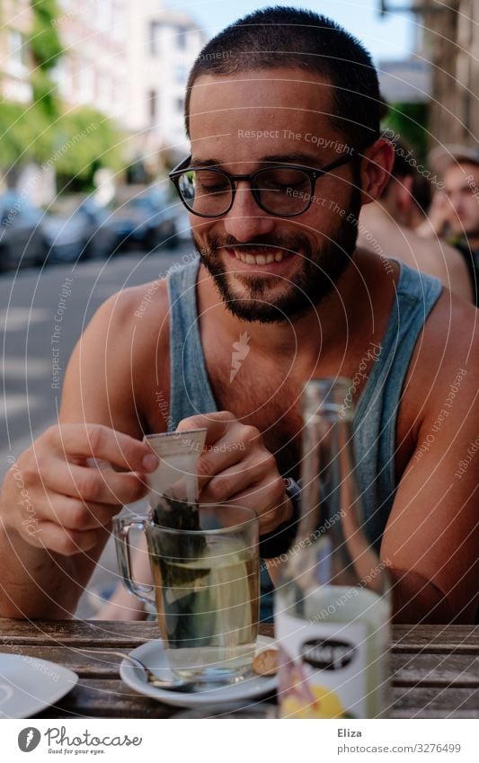 Ein Mann der draußen im Sommer in einem Café sitzt und einen Tee trinkt und lächelt Mensch maskulin Junger Mann Jugendliche Erwachsene Lächeln Außenaufnahme