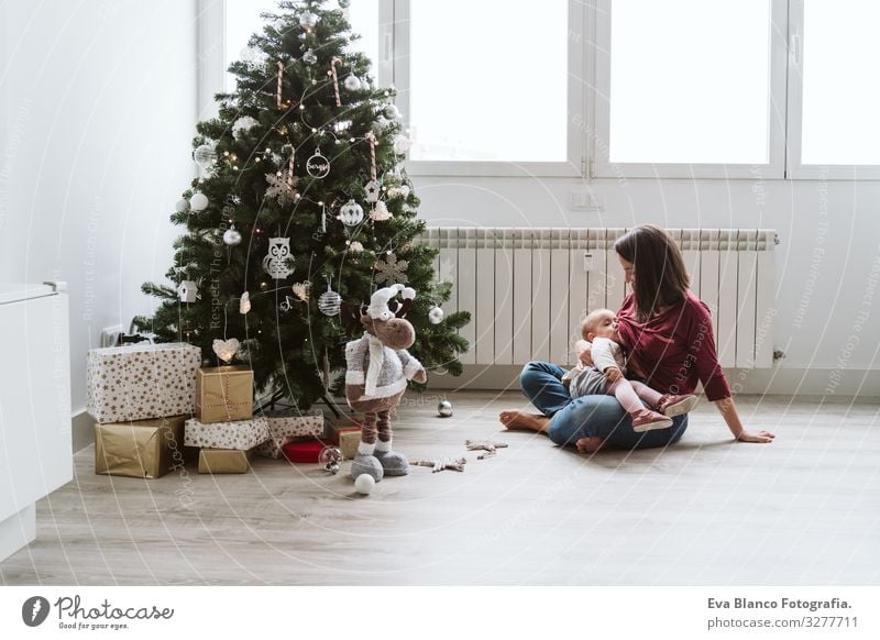 Mutter, die ihr Kind am Weihnachtsbaum stillt stillen Fressen Essen natürlich Lebensmittel Mutterschaft Glück niedlich Baby Mädchen ein Jahr dekorierend