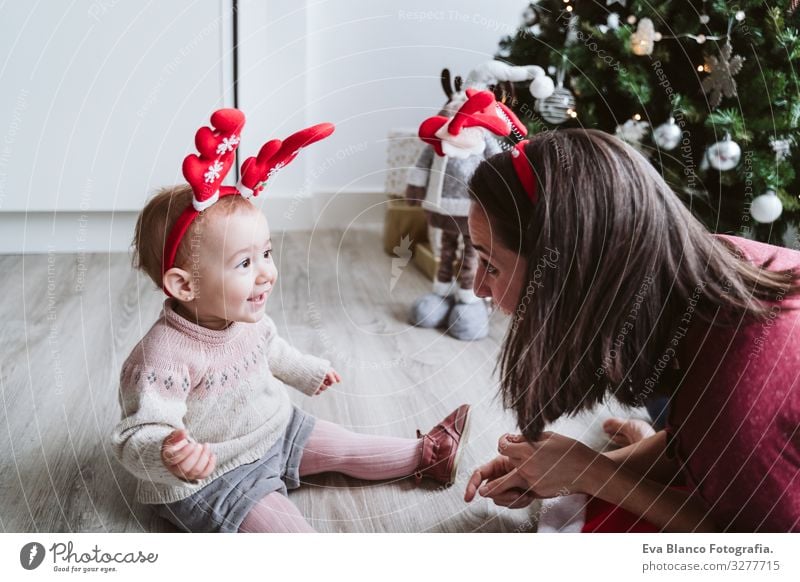 Mutter und süßes Mädchen spielen zu Hause mit einem Rentierdiadem. Weihnachts-Konzept Spielen Diadem Weihnachtsmann Mutterschaft Glück niedlich Baby ein Jahr