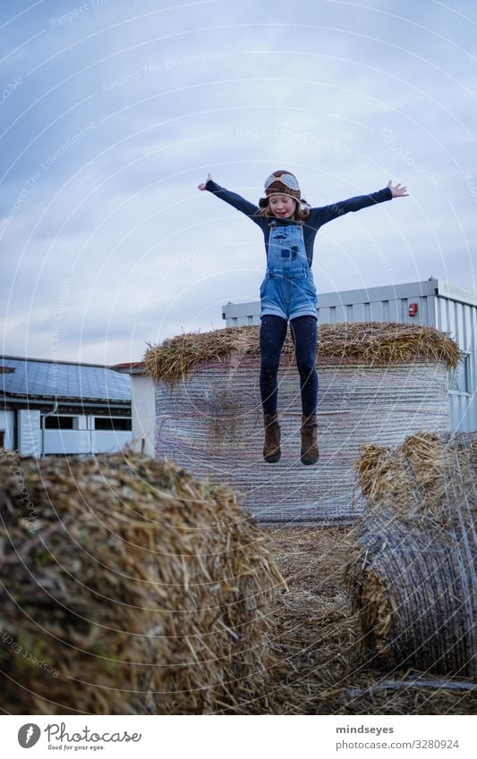 Mädchen mit Latzhose und Fliegermütze springt ins Stroh Freude Freizeit & Hobby Spielen Abenteuer Kind Kindheit 1 Mensch 3-8 Jahre Wolken Strohballen Dorf