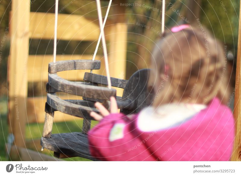 Kleinkind steht vor leerer Schaukel und schubst sie an. Kinderspiel Mensch feminin 1 1-3 Jahre schaukeln Holz anschubsen anschieben Hand wollwalk Haarspange