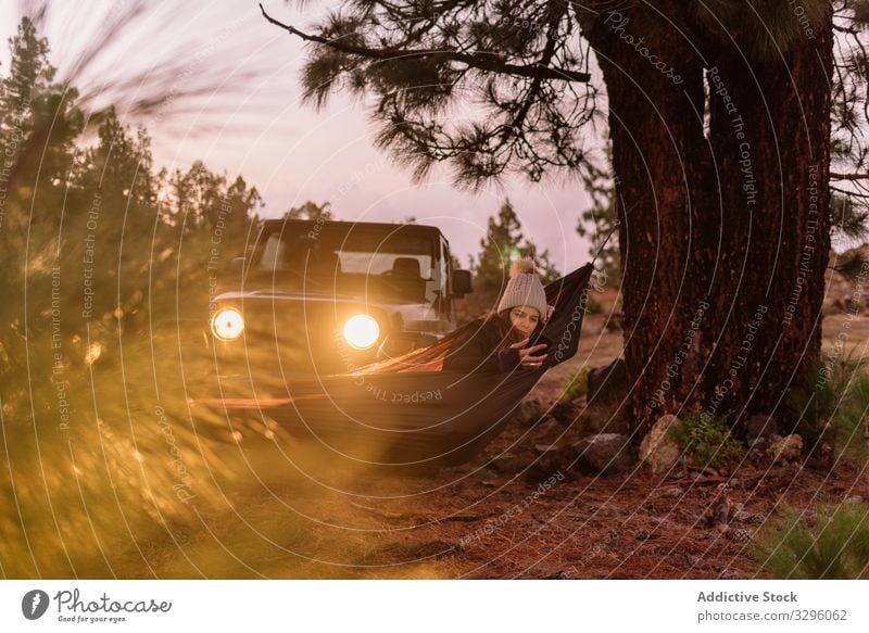 Warm gekleidete Frau in Hängematte am Baum im Scheinwerferlicht des Autos reisend PKW aussruhen Smartphone Apparatur Wald Genuss Spaß haben Browsen Surfen