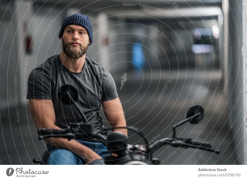 Bärtiger Biker im Garagenflur Motorrad Mann modern sitzen selbstbewusst bärtig Verkehr Mitfahrgelegenheit männlich Fahrzeug Großstadt urban Flur Gang