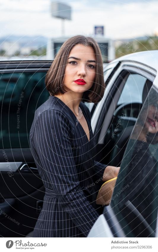 Emotionsloses weibliches Modemodel in modischer Kleidung in der Nähe des Autos auf der Straße Frau trendy PKW stylisch Bekleidung Großstadt Stehen jung Dame