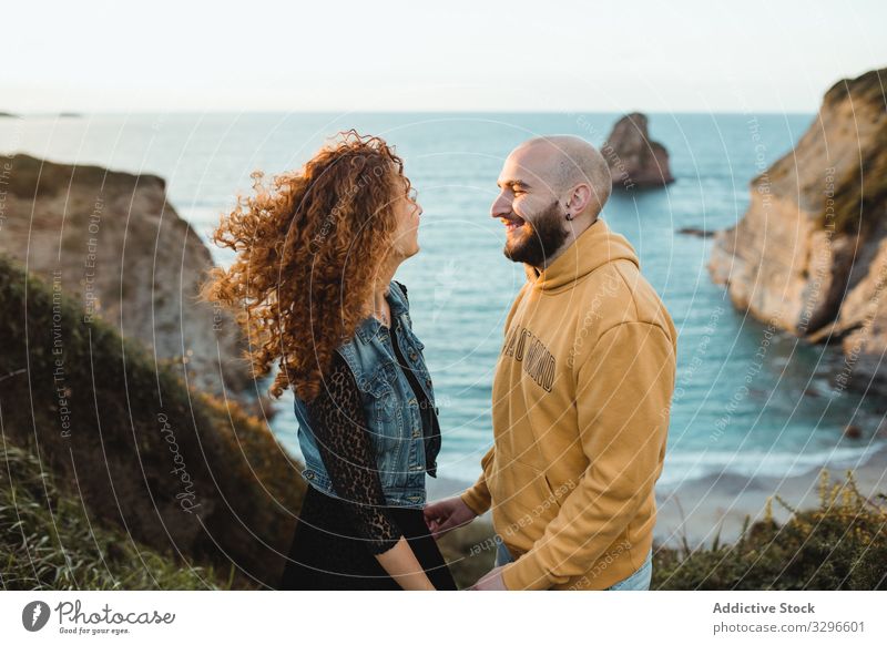 Fröhliches verliebtes Paar am Meer stehend romantisch Meeresufer Glück Liebe Felsen Klippe Natur Ufer Hipster Meereslandschaft jung Zusammensein reden Seeküste