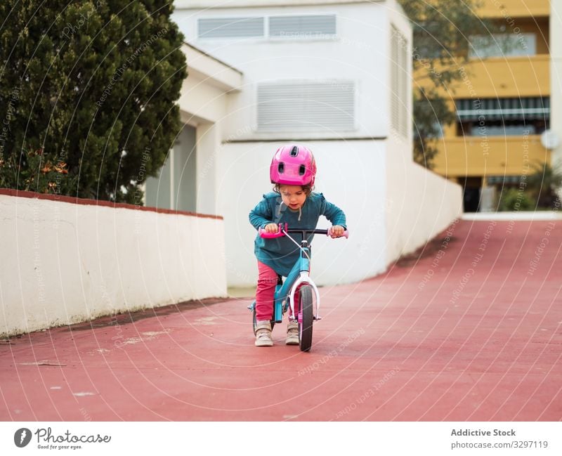 Kleines Mädchen auf Fahrrädern Kind Fahrrad Mitfahrgelegenheit Hof Straße Großstadt Rollschuhe Sicherheit Schutz Schutzhelm Weg Gebäude Außenseite Sommer Saison