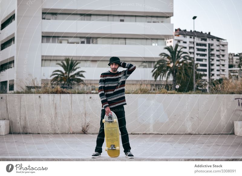 Junger stilvoller Mann mit Skateboard in der Stadt stehend Schlittschuh Straße Großstadt Gebäude Hipster stylisch jung modern Zeitgenosse aktiv männlich urban