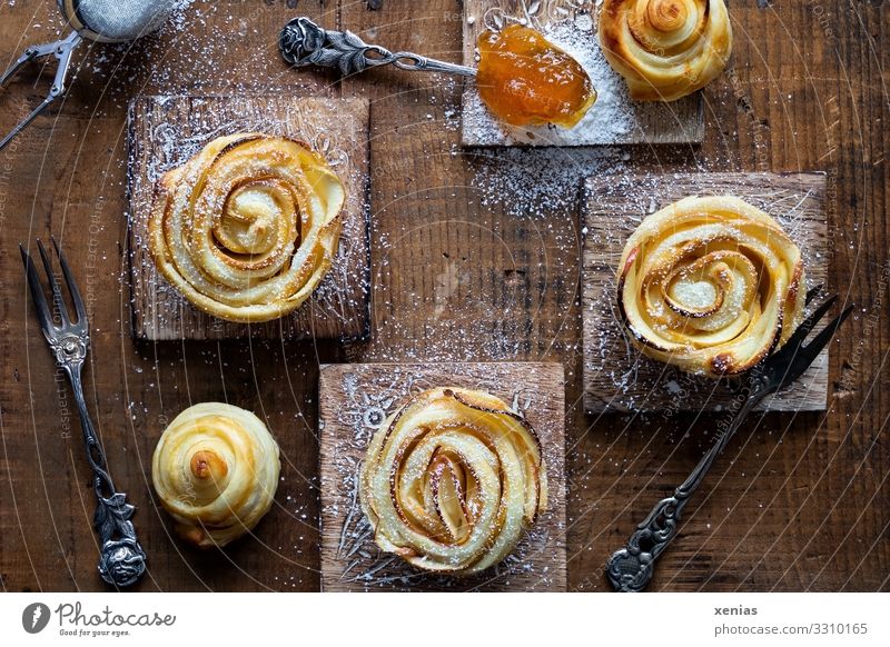 Drei Apfelrosen mit Puderzucker und Aprikosenmarmelade auf Holzbrettchen Lebensmittel Teigwaren Backwaren Kuchen Marmelade Aprikosenkonfitüre Ernährung