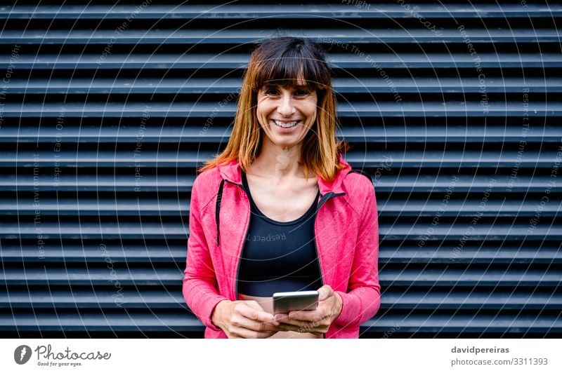 Glückliche Sportlerin mit Mobiltelefon Lifestyle Handy PDA Mensch Frau Erwachsene brünett Fitness Lächeln stehen sportlich dünn Freundlichkeit schwarz