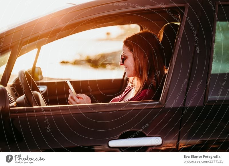 junge Frau, die bei Sonnenuntergang Auto fährt und ein Mobiltelefon benutzt. reisekonzept Jugendliche PKW fahren Strand Fahrer Ferien & Urlaub & Reisen reisend