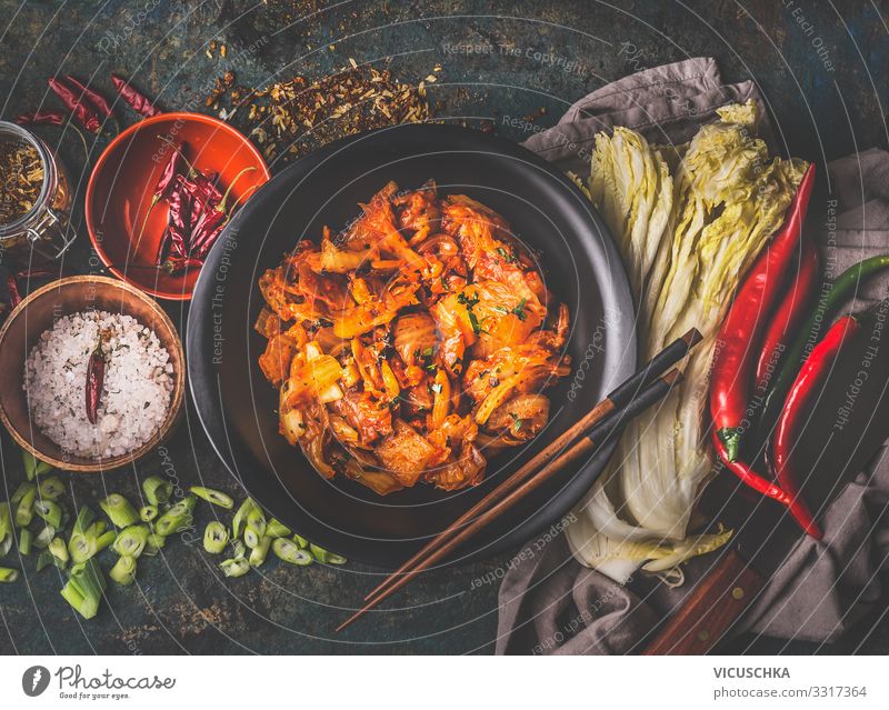 Hausgemachte Kimchi in schwarzer Schale auf rustikalem Hintergrund mit Zutaten: Chinakohl , Chili, Gewürze und Salz . Ansicht von oben. Gesundes fermentiertes Essen