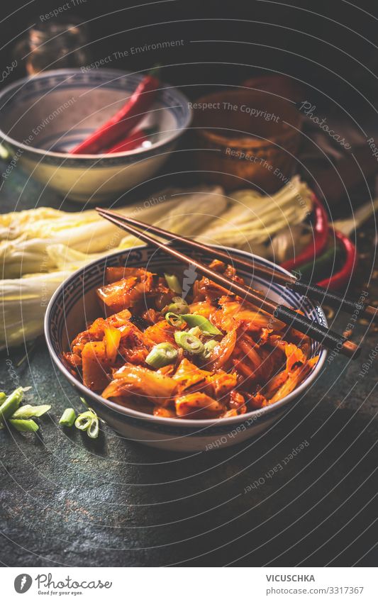 Kimchi, fermentierter Chinakohl in scharfer Chilisauce , in Schale mit Stäbchen auf rustikalem Küchentisch. Nahaufnahme Selleriekohl heiß Peperoni Saucen