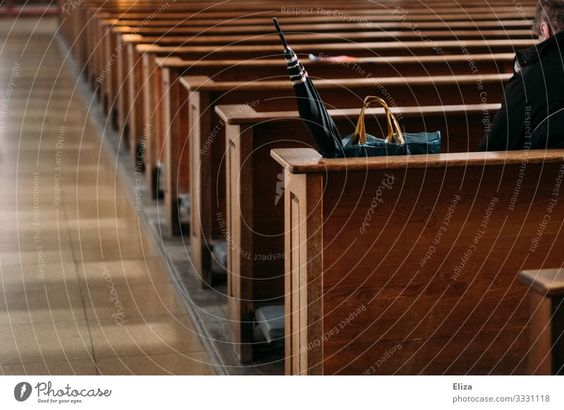 Ein Mann sitzt einsam und alleine neben seinem Regenschirm und Einkaufstasche auf einer Kirchenbank in der Kirche und betet Mensch beten sitzen Bank Einsamkeit