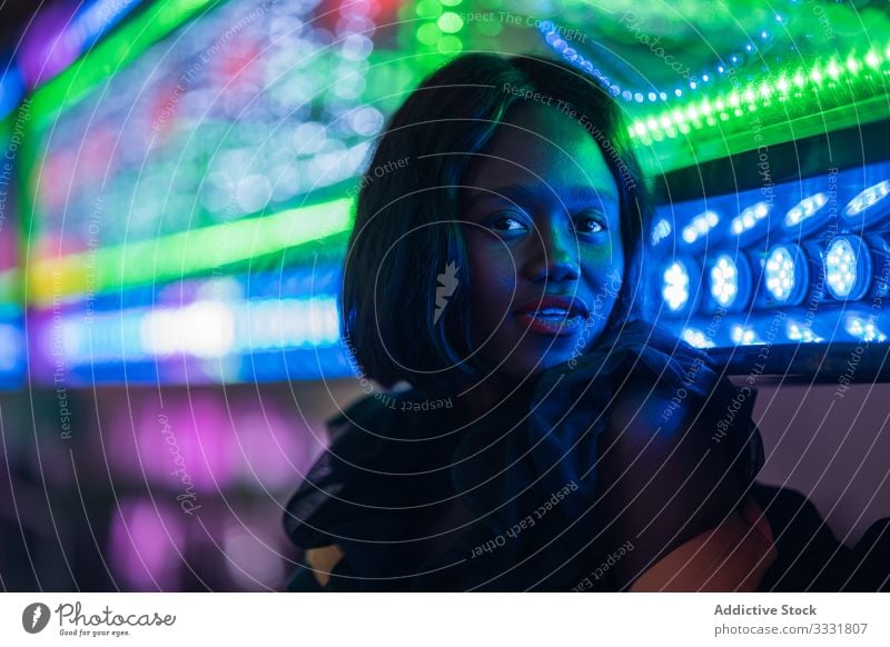 Fröhliche schwarze Frau auf Rummelplatz Jahrmarkt Lächeln Nacht Arkaden Illumination sitzen ruhen Wochenende ethnisch Vergnügen Anziehungskraft farbenfroh