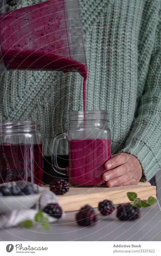 Koch gießt in zeitgenössischer Küche leckeres gesundes Getränk aus Beerenmix und Minze aus dem Mixer in einen durchsichtigen Krug Smoothie mischen Frucht