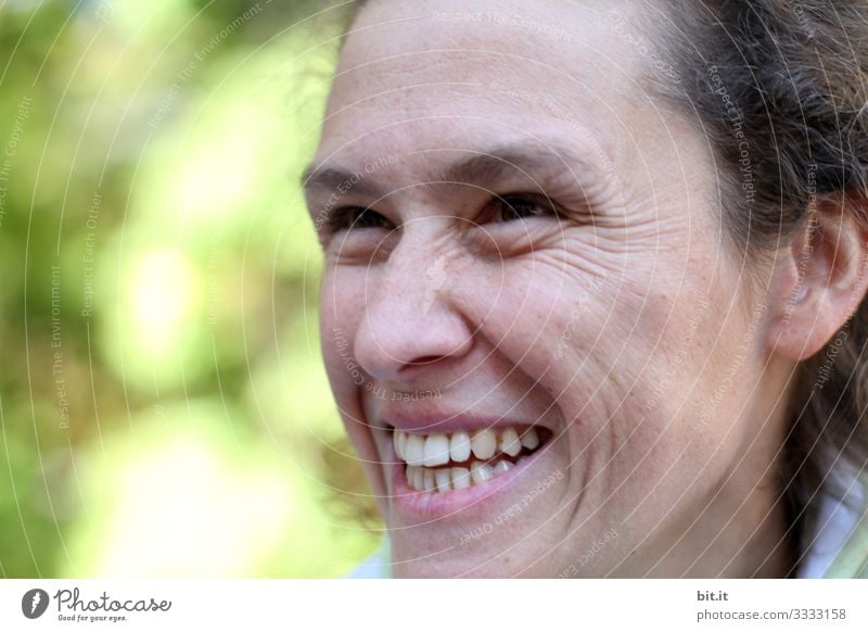 Junge, natürliche, symphatische, authentische Frau schaut nach oben und lacht herzhaft. Fröhliche Frau mit Lachfältchen draussen in der Natur vor grün-gelben, leuchtendem Bokeh. Optimistische, neugierige, fröhliche, feminine Person schaut lachend hoch.