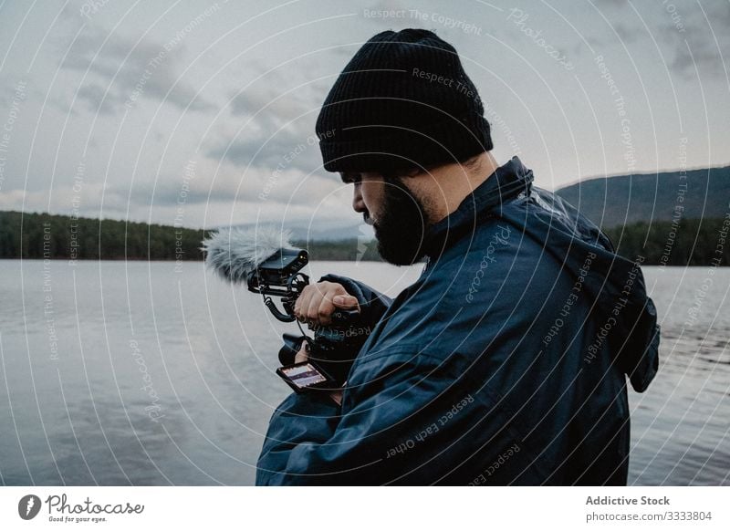 Fokussierter Mann betrachtet Fotos vor der Kamera benutzend Fotokamera Videofilmer überblicken Fluss Wald Natur fokussiert beschäftigt ernst Strand männlich