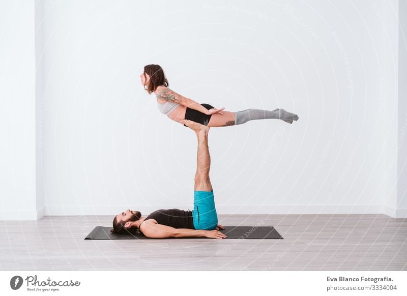 junges Paar, das in einem weißen Studio oder einer Sporthalle Akro-Yoga praktiziert. Gesunder Lebensstil im Innenbereich Gesundheit Mann Kraft Mensch