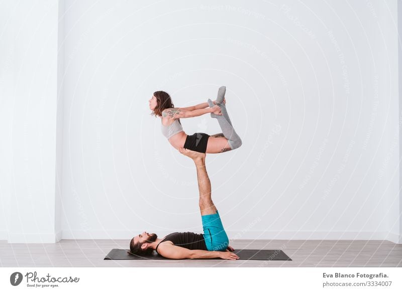 junges Paar, das in einem weißen Studio oder einer Sporthalle Akro-Yoga praktiziert. Gesunder Lebensstil im Innenbereich Gesundheit Mann Kraft Mensch