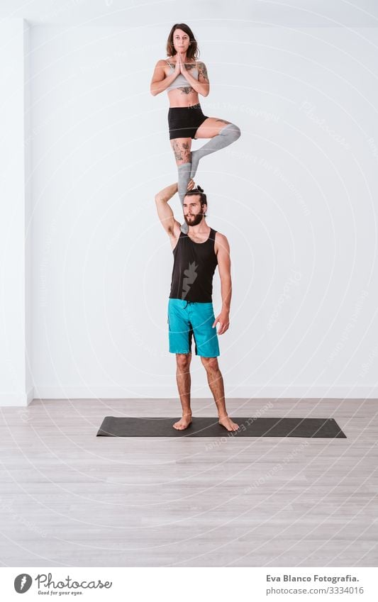 junges Paar, das in einem weißen Studio oder einer Sporthalle Akro-Yoga praktiziert. Gesunder Lebensstil im Innenbereich Gesundheit Mann Kraft Mensch