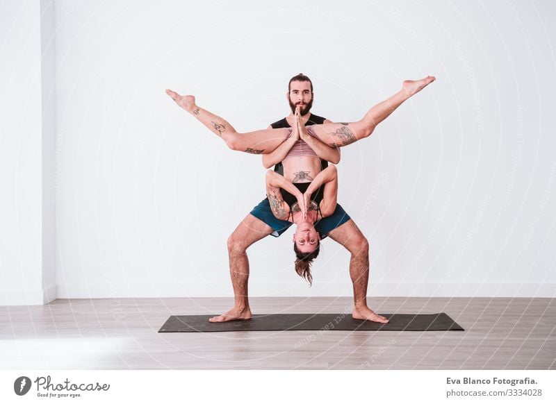 junges Paar, das in einem weißen Studio oder einer Sporthalle Akro-Yoga praktiziert. Gesunder Lebensstil im Innenbereich Gesundheit Mann Kraft Mensch