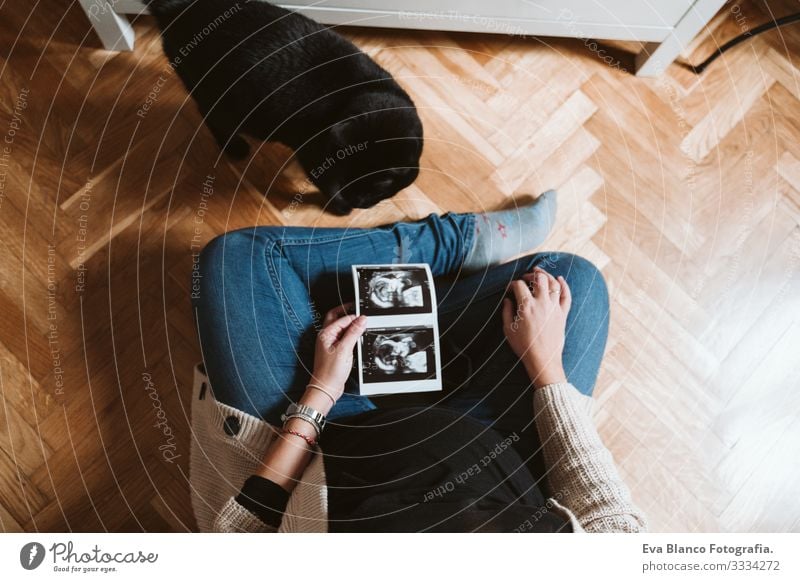 junge schwangere Frau zu Hause mit schwarzer Katze, die ein Ultraschallbaby hält schwarze Katze Jugendliche Schwangerschaft heimwärts Mutterschaft Leben