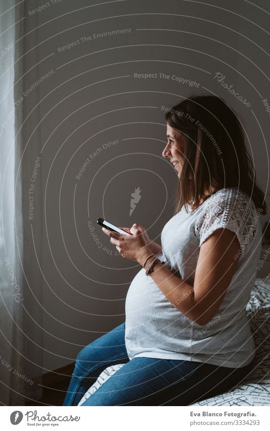 junge schwangere Frau zu Hause, die ein Mobiltelefon benutzt heimwärts Handy Technik & Technologie PDA Lächeln bauchfrei dick Baby erwartend Innenaufnahme