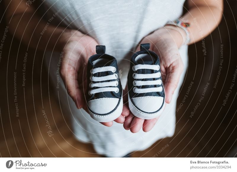 junge schwangere Frau zu Hause, die Babyschuhe hält heimwärts Bett Schwangerschaft erwartend bauchfrei Tag liegen Zärtlichkeit Vergnügen Innenarchitektur