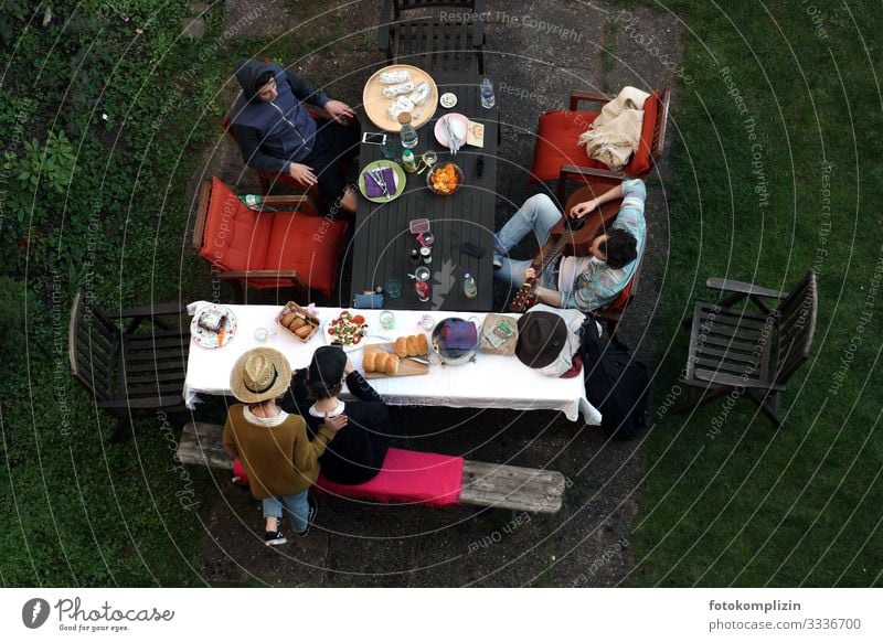 Blick von oben auf vier Menschen mit Picknick und Gitarrenspieler am Gartentisch chillen Zusammensein ruhig Gemeinschaft Siesta Gartenidylle Gitarre spielen