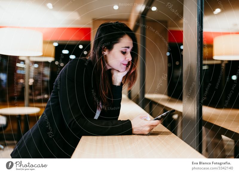 eine junge Frau, die in einem Café oder Restaurant in Innenräumen ein Mobiltelefon benutzt. Technologie und Lebensstil Handy Innenaufnahme Fenster Geschäftsfrau