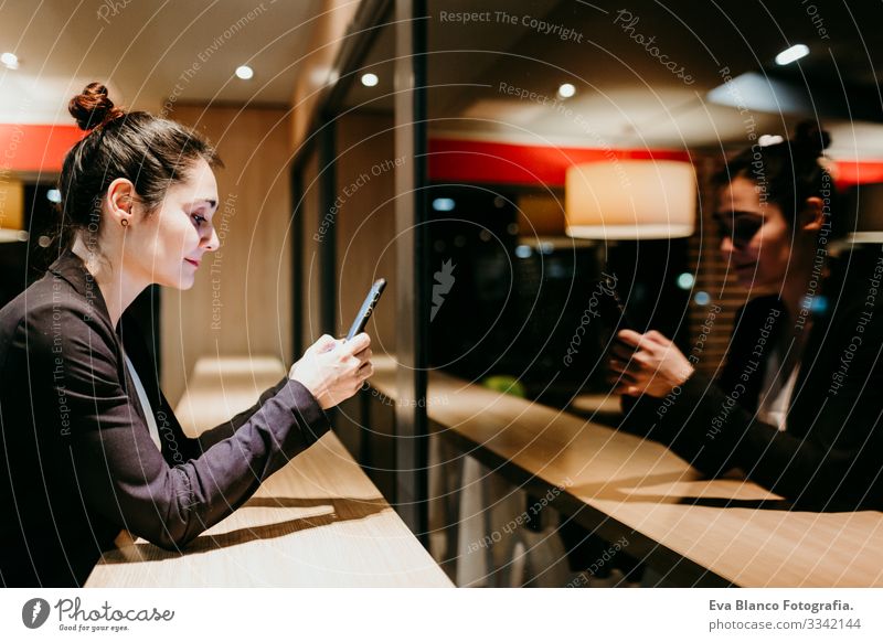 eine junge Frau, die in einem Café oder Restaurant in Innenräumen ein Mobiltelefon benutzt. Technologie und Lebensstil Handy Innenaufnahme Fenster Geschäftsfrau