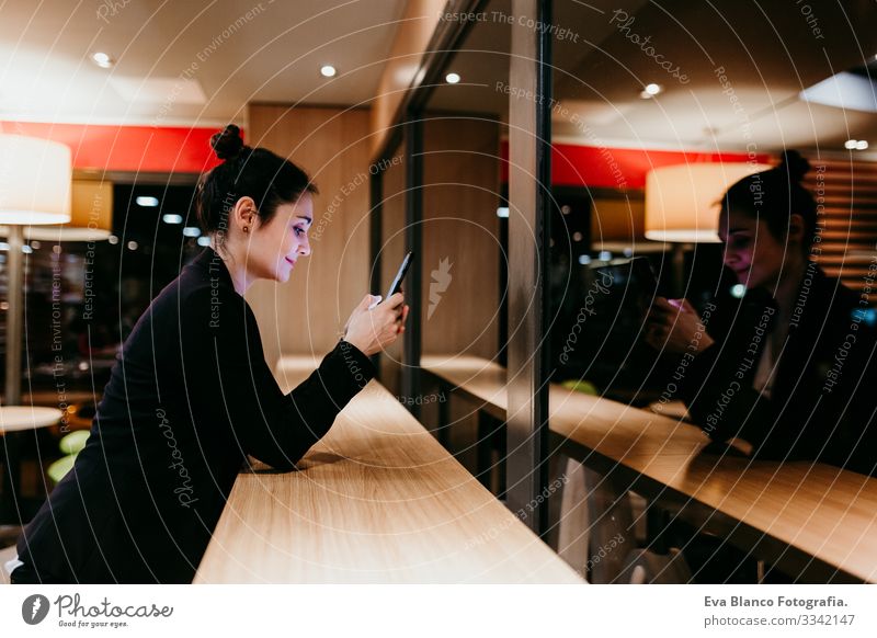 eine junge Frau, die in einem Café oder Restaurant in Innenräumen ein Mobiltelefon benutzt. Technologie und Lebensstil Handy Innenaufnahme Fenster Geschäftsfrau