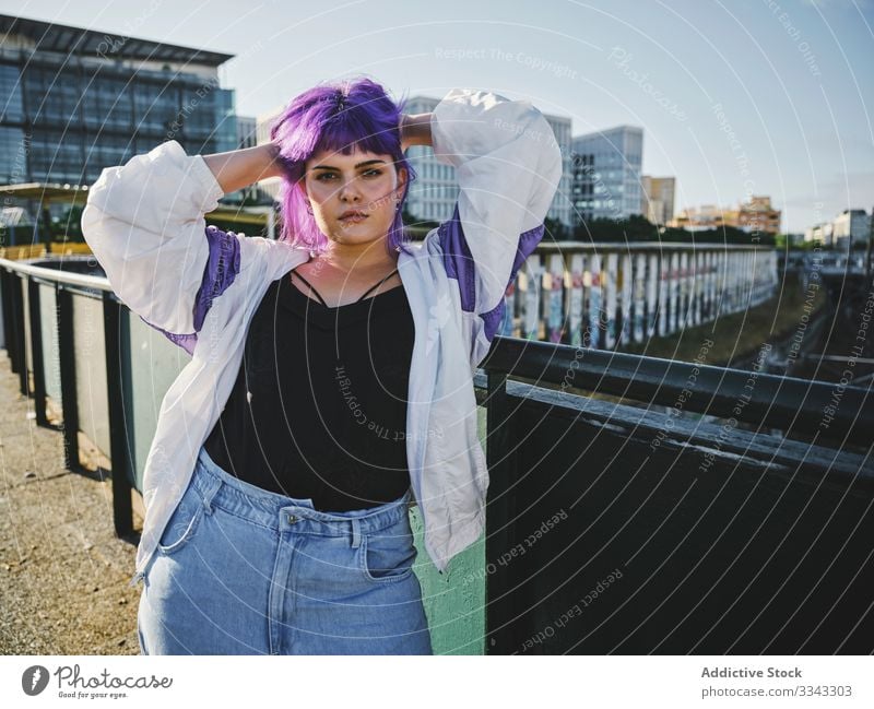 Frau mit violettem Haar lehnt an Metallzaun Lehnen berührend stylisch urban purpur Frisur Jacke glänzend Zaun Revier selbstbewusst Mode jung Stil Model Straße