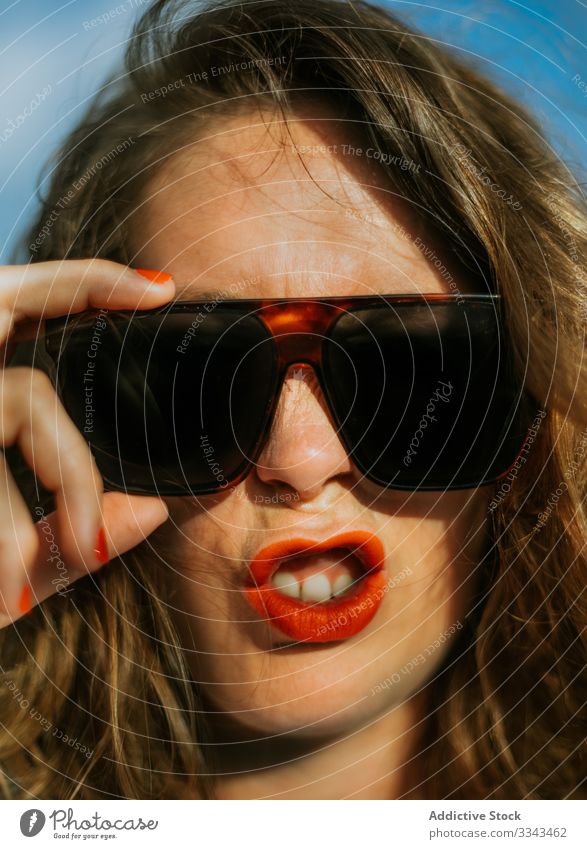 Zeitgenössische ruhende Dame, die ihr Gesicht berührt Frau Sonnenbrille Stil Lippenstift rot modisch Zeitgenosse Hände Handflächen jung Urlaub reisen Frisur